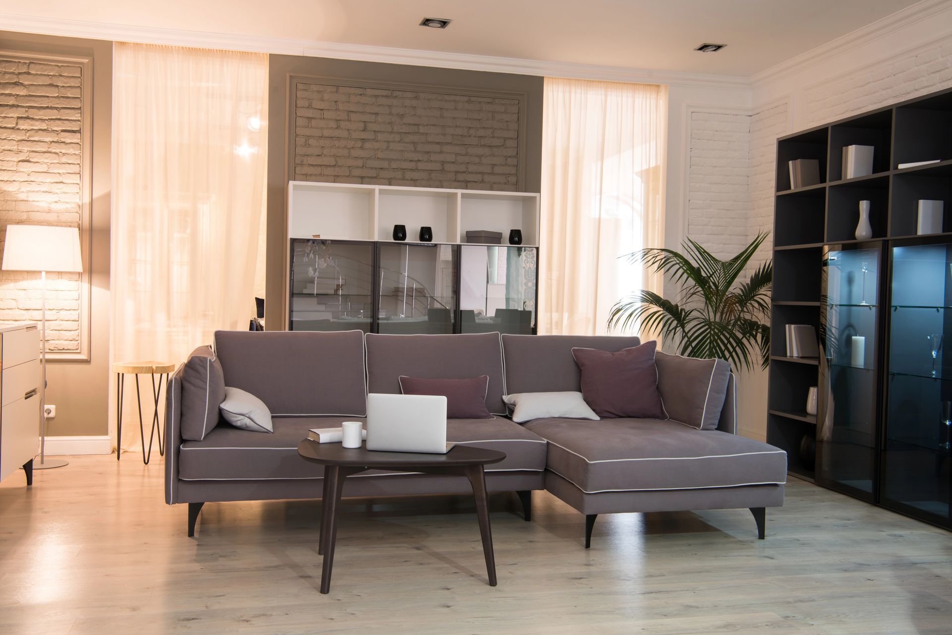 Soggiorno moderno con divano grigio, tavolino da caffè, mensole a vista e calda luce naturale.