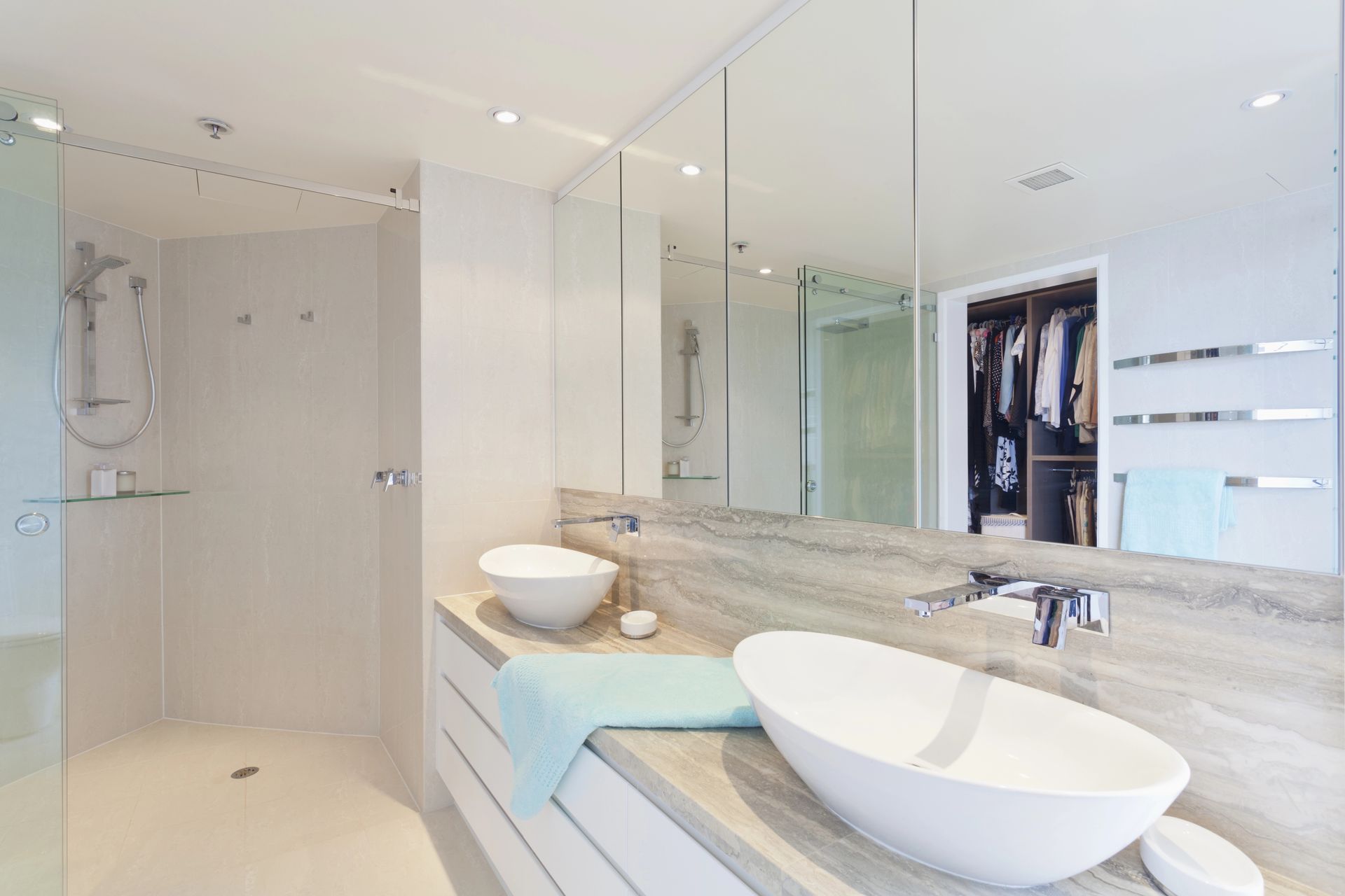 Luminoso bagno moderno con doppio lavabo a ciotola, ampio specchio, doccia in vetro e ripiani in marmo.