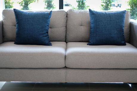 Divano beige con due cuscini decorativi blu in un luminoso soggiorno.