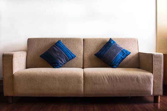 Divano beige con due cuscini a righe blu, appoggiato a una parete bianca, in una stanza luminosa.