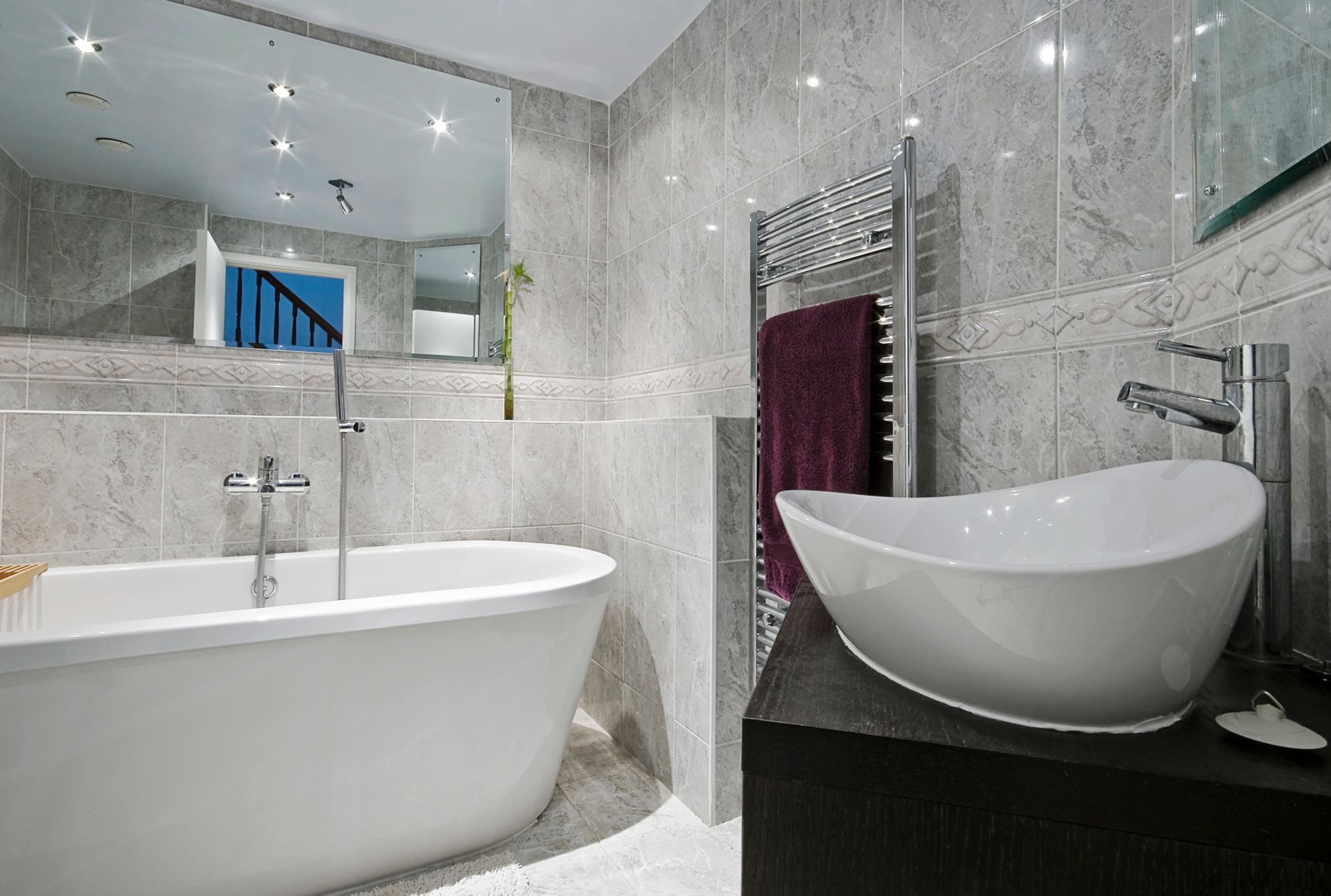 Bagno moderno con vasca freestanding, lavabo a bacinella, parete a specchio e piastrelle in marmo grigio.