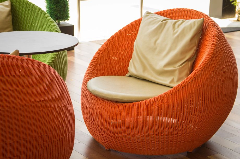 Poltrona lounge arancione intrecciata con cuscini beige in una luminosa zona salotto interna.