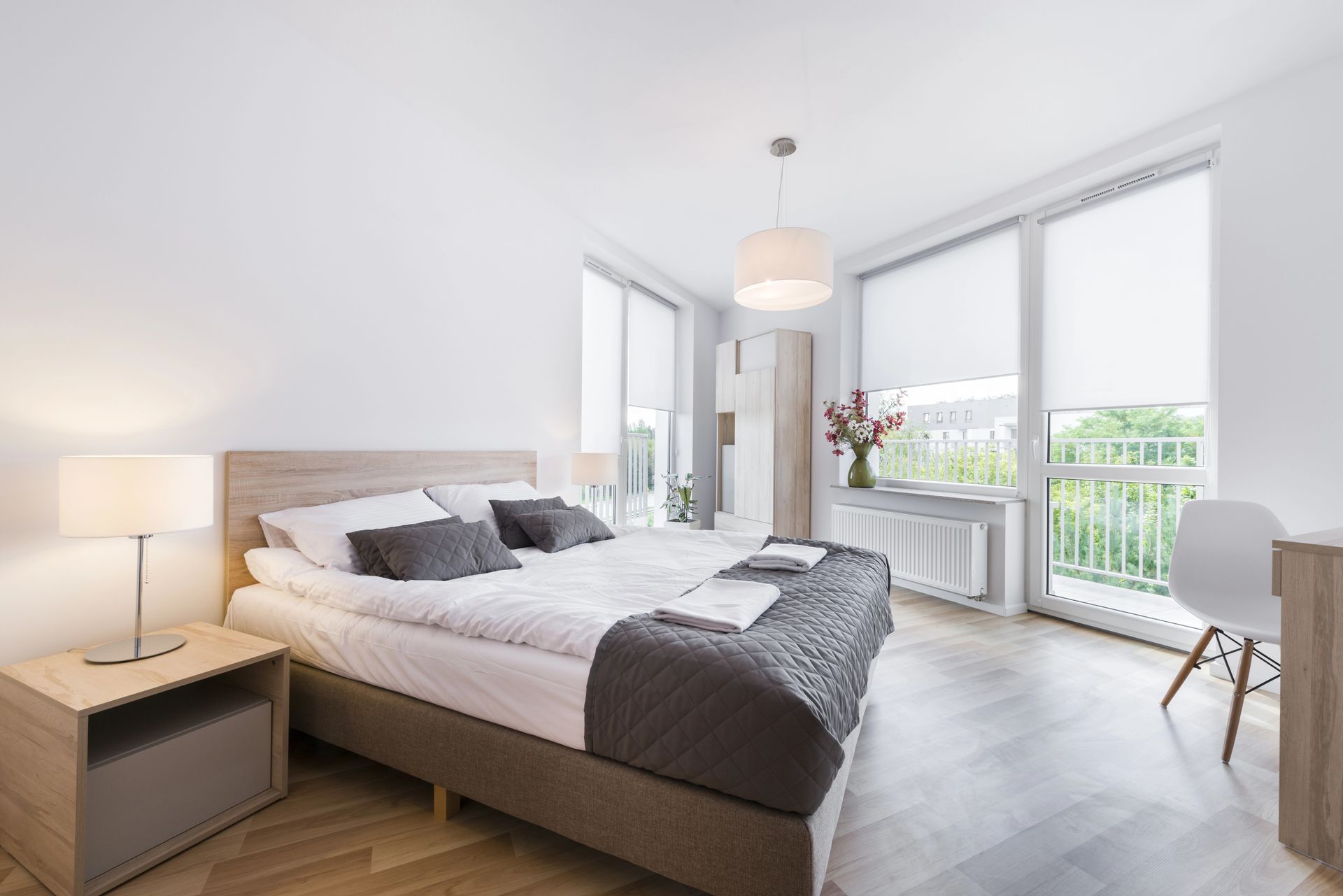 Luminosa camera da letto moderna con un ampio letto, lampada da comodino e finestre che si affacciano su un balcone.