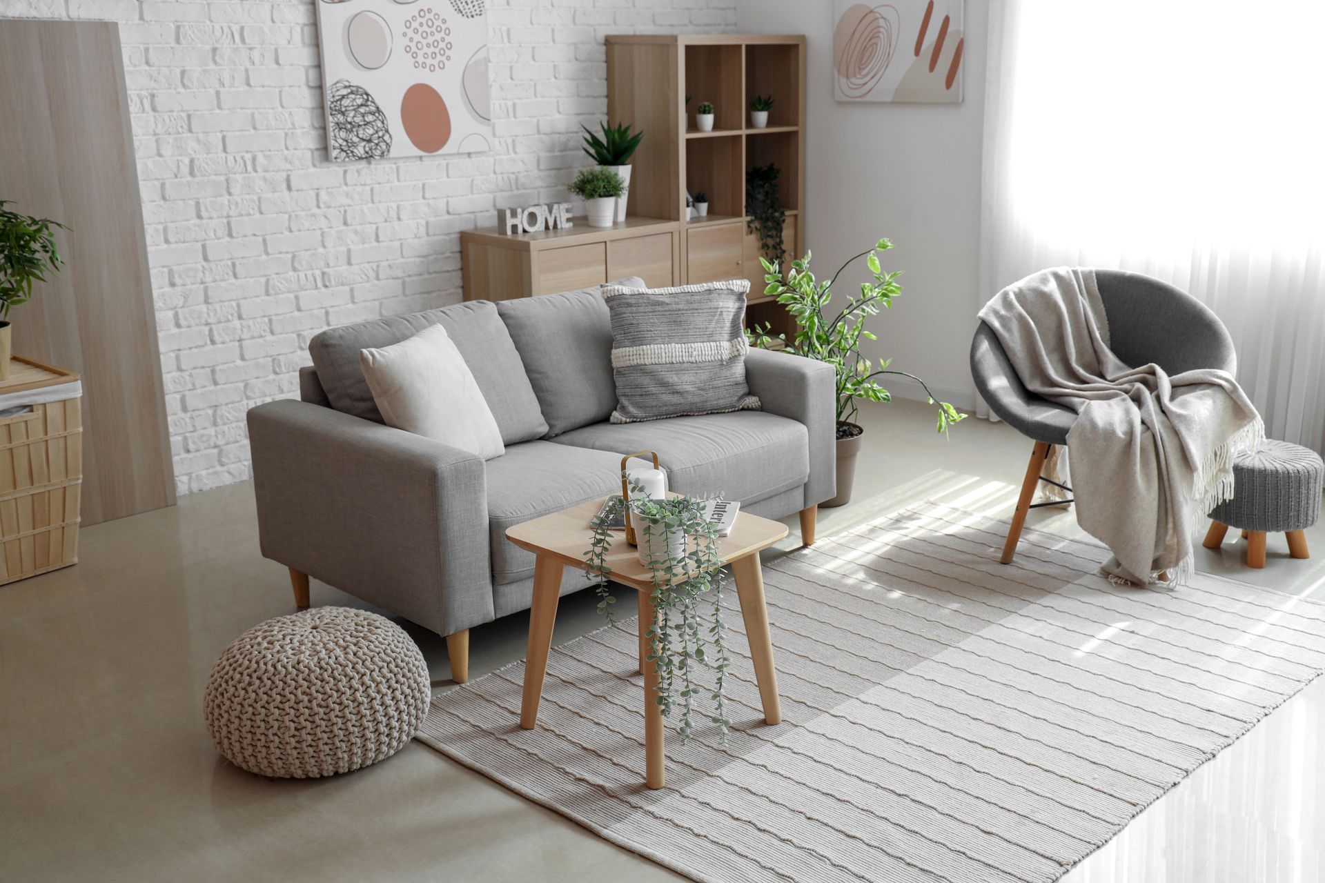 Accogliente soggiorno con divano grigio, tappeto a righe, poltrona rotonda e dettagli decorativi in ​​legno chiaro.