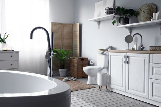 Bagno moderno bianco con vasca freestanding, mobile lavabo, WC e piante vicino alla finestra.