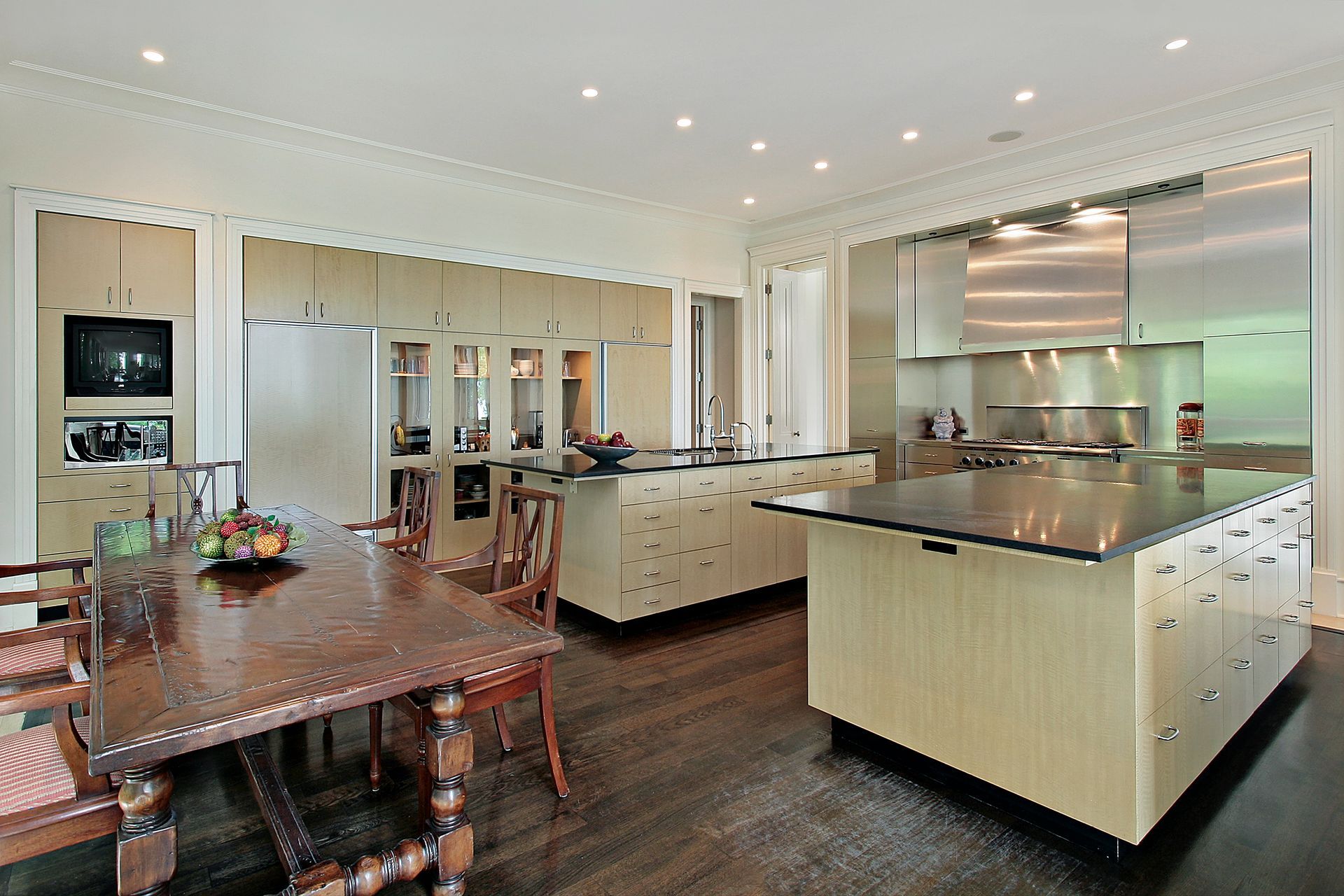 Cucina moderna e zona pranzo con grande isola, tavolo in legno ed elettrodomestici in acciaio inossidabile.