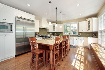 Cucina luminosa con isola, sgabelli in legno, frigorifero in acciaio inox, mobili bianchi e luce naturale sul pavimento.