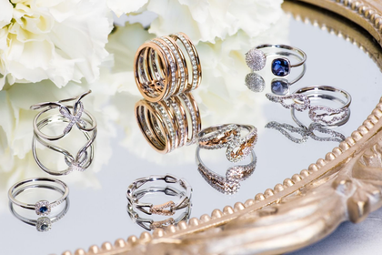 Assorted silver and gold rings arranged on a mirrored tray with white flowers nearby