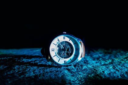Glowing white clock face on a dark blue textured surface in a dark, moody setting
