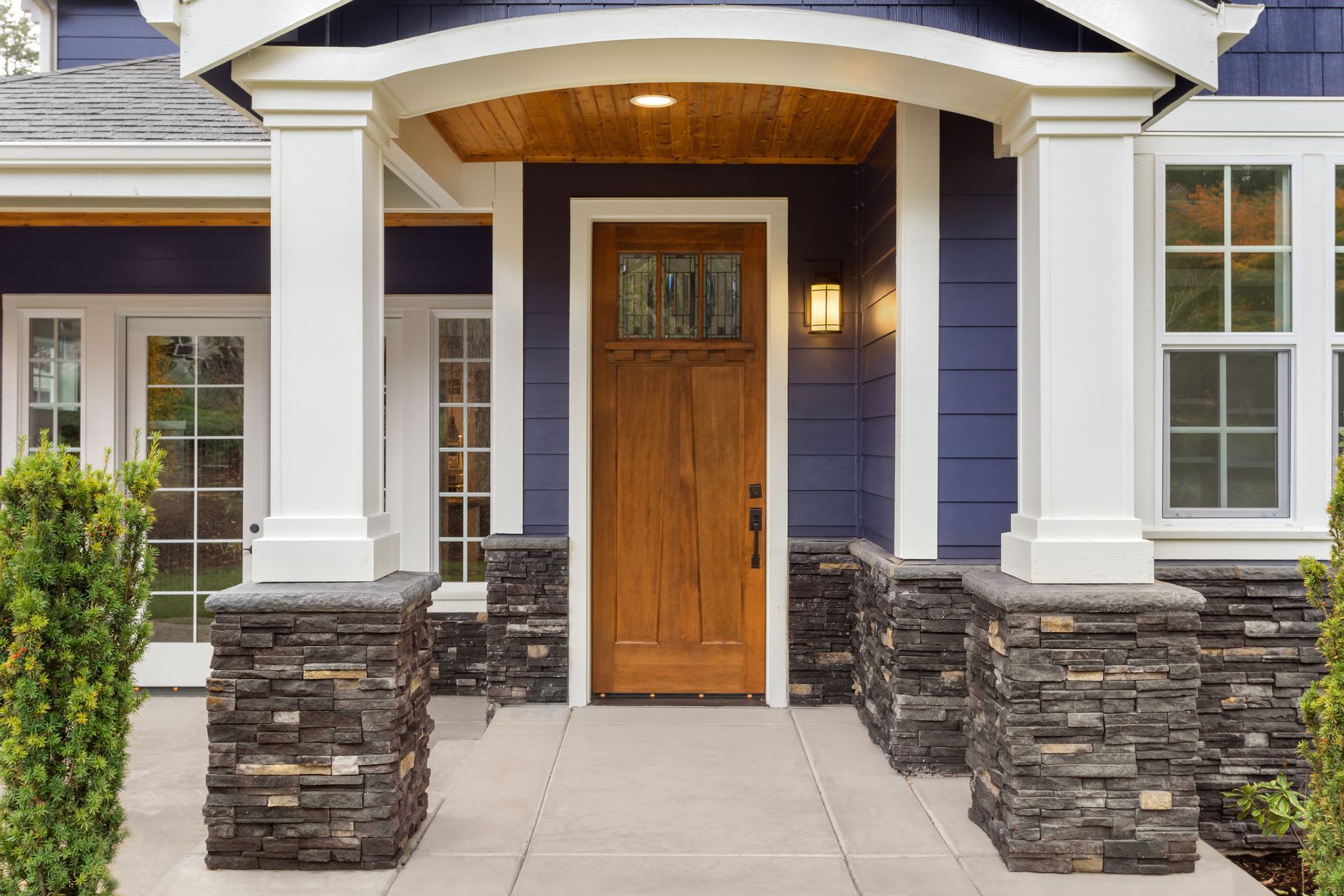 Wooden front door of a blue house with white pillars and stone accents.