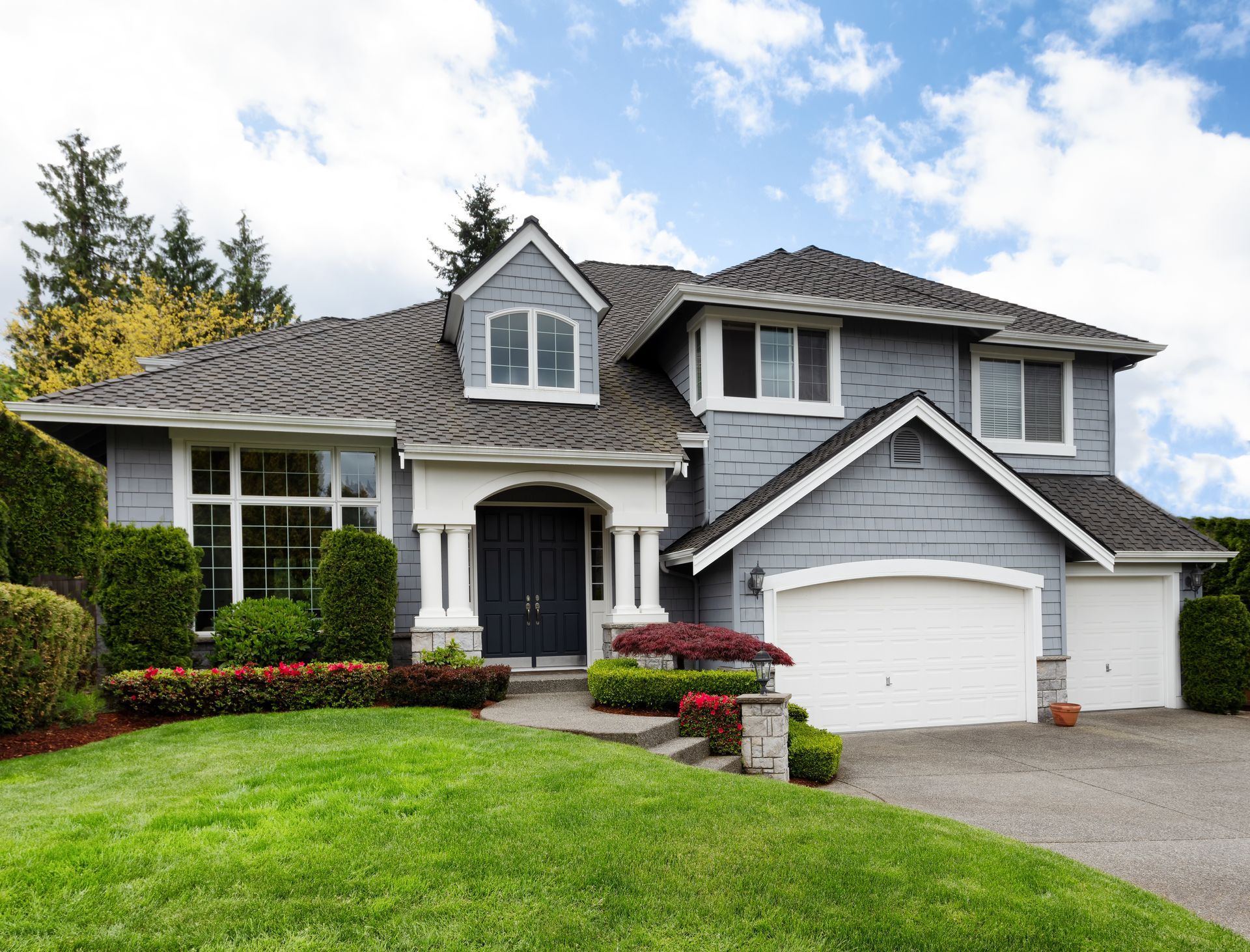 Gray house with a two-car garage, manicured lawn, and colorful landscaping.