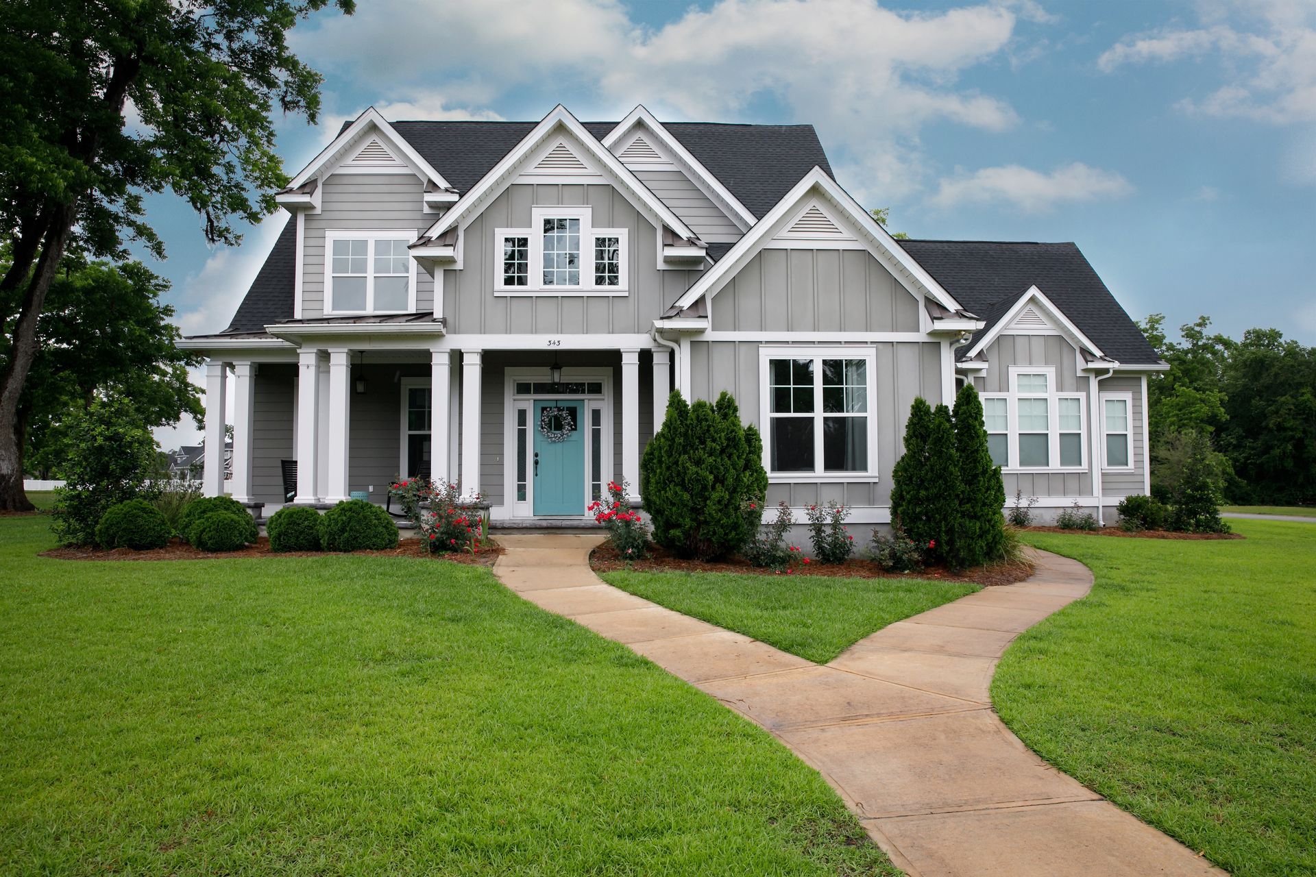 Gray two-story house with blue door, white trim, and a split walkway through green lawn under a cloudy sky. Gray two-story house with blue door, white trim, and a split walkway through green lawn under a cloudy sky.