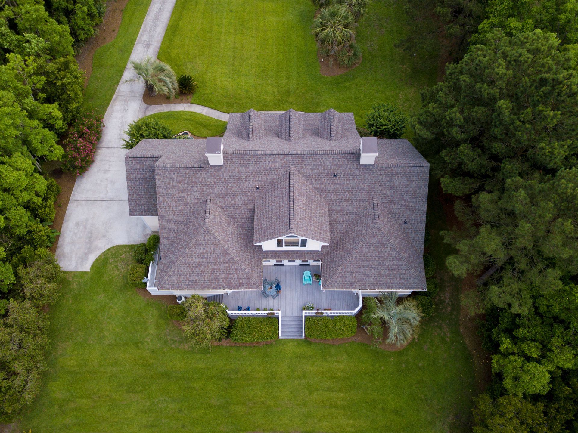 Aerial view of a house with a gray roof and white trim surrounded by green grass and trees.