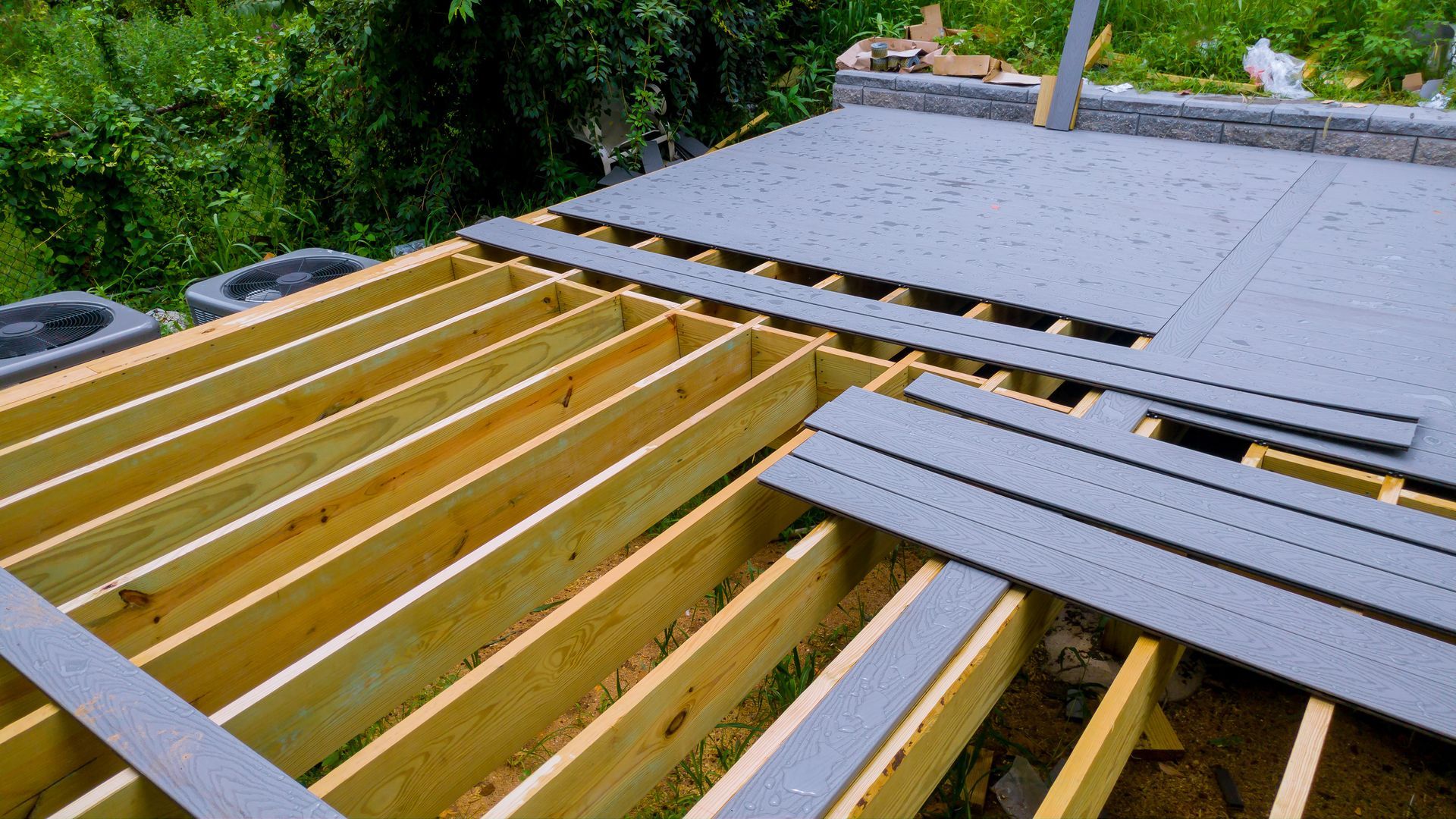 Deck construction: wooden frame with gray composite decking boards partially installed, outdoor setting.