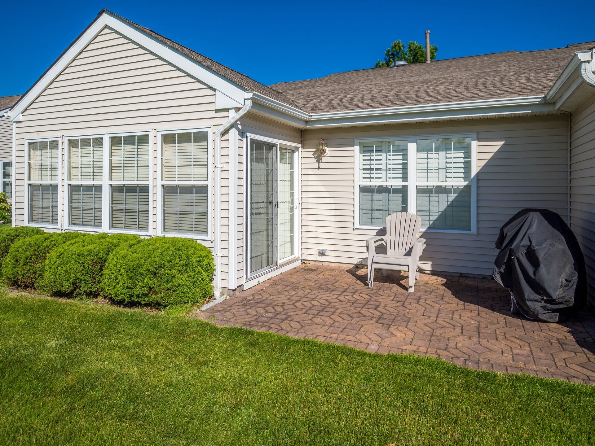 Backyard patio with a chair, grill cover, and green lawn. Backyard patio with a chair, grill cover, and green lawn.