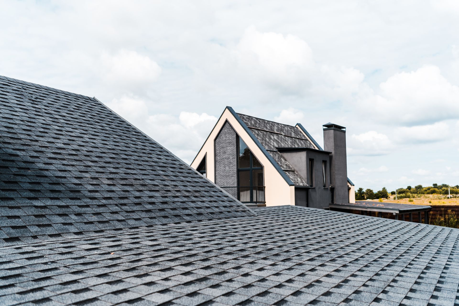 Gray shingled rooftops, with a modern gray and white house in the background. Cloudy sky. Gray shingled rooftops, with a modern gray and white house in the background. Cloudy sky.