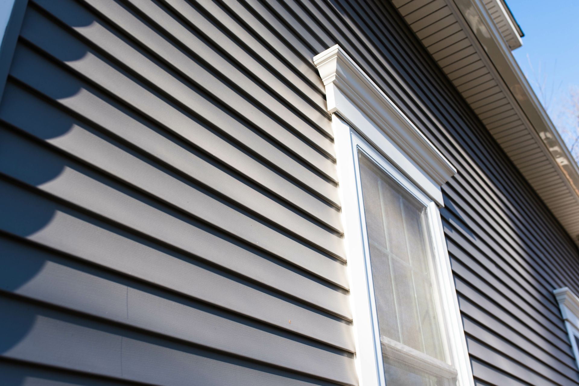 Gray siding on a house, window with white trim, and sunlight.