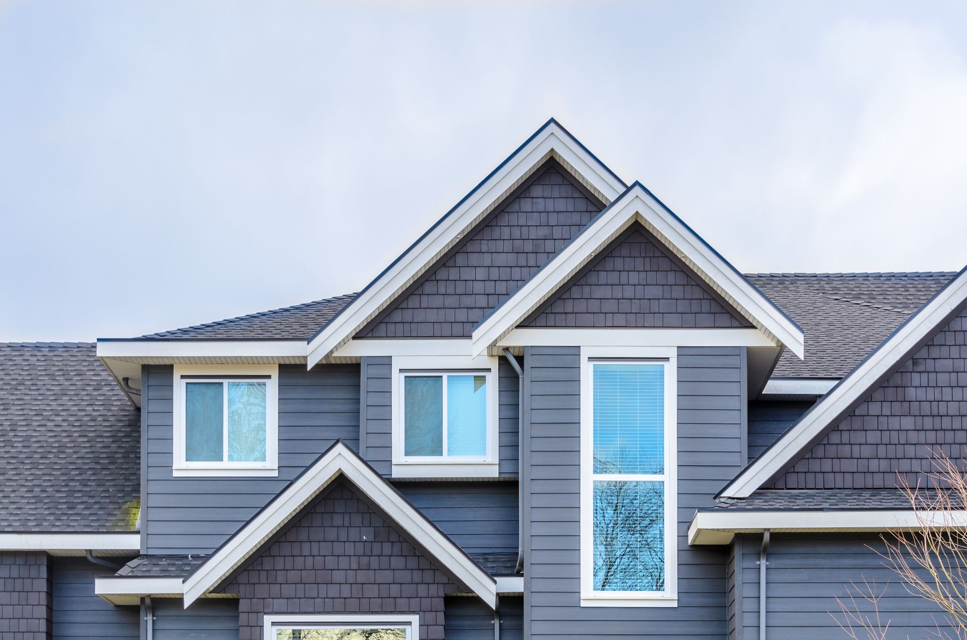 Gray house with multiple gabled rooflines, dark gray siding, and white-trimmed windows. Gray house with multiple gabled rooflines, dark gray siding, and white-trimmed windows.