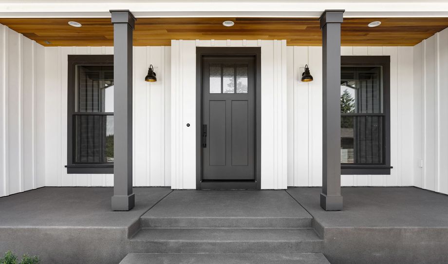 Gray front door with sidelights, porch with columns, and board-and-batten siding. Gray front door with sidelights, porch with columns, and board-and-batten siding.