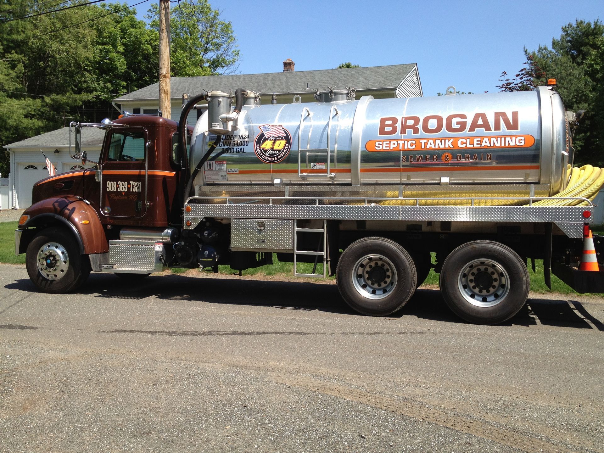 Red tanker truck with “BROGAN” logo parked on a roadside under trees