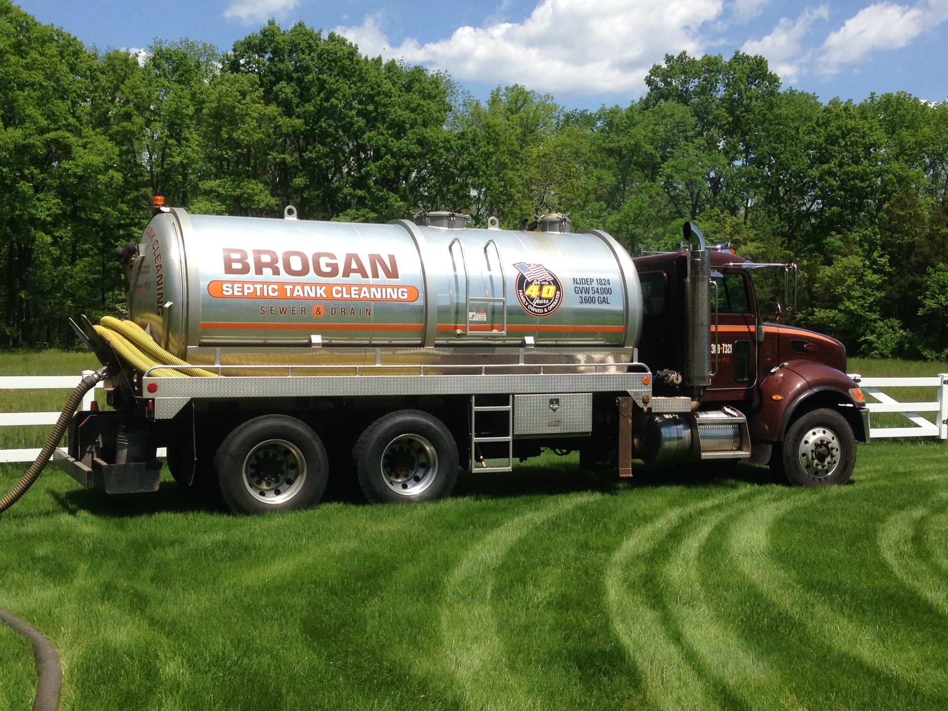 Brogan septic service truck parked on green lawn with trees and blue sky