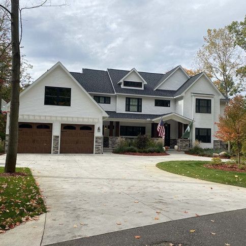 A large white house with a black roof and brown garage doors.