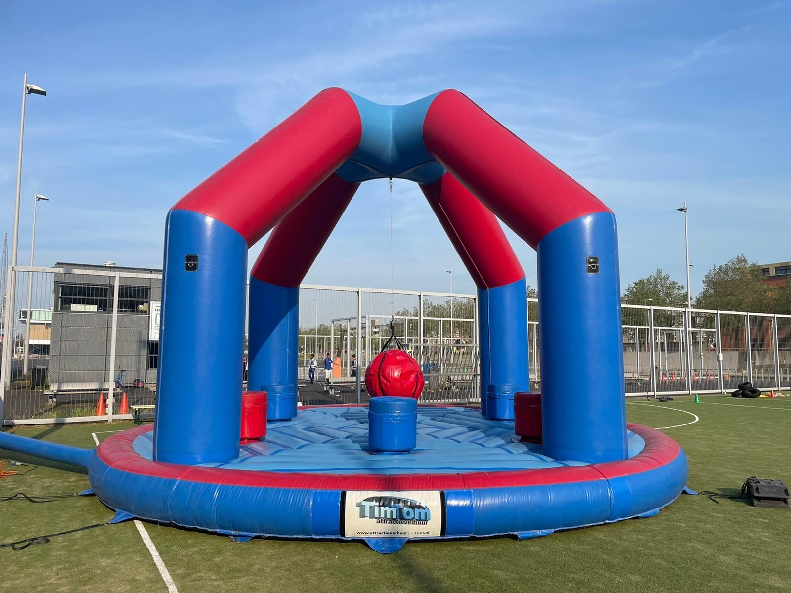 Opblaasbare rode en blauwe speelarena op een groen veld onder een blauwe hemel.