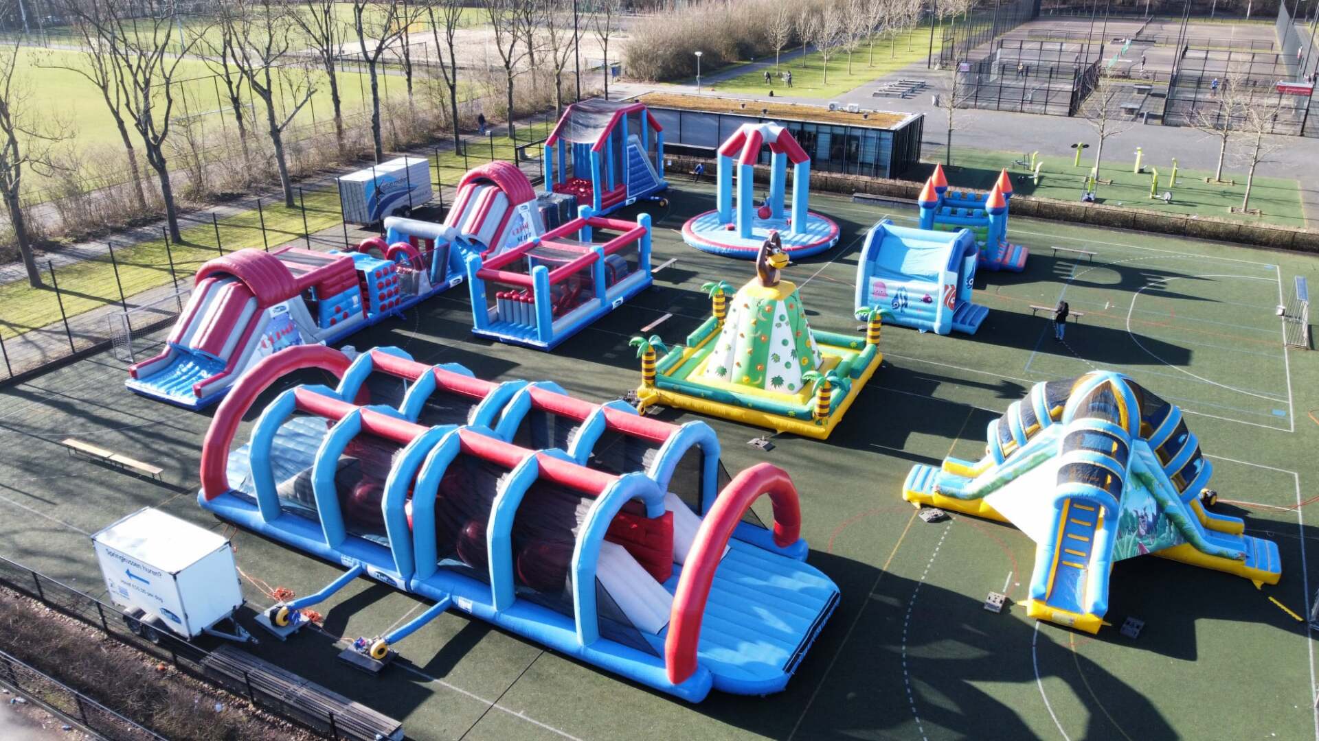Een opblaasbaar hindernisparcours, buiten op een kunstgrasveld opgesteld. De constructies hebben verschillende vormen en kleuren.