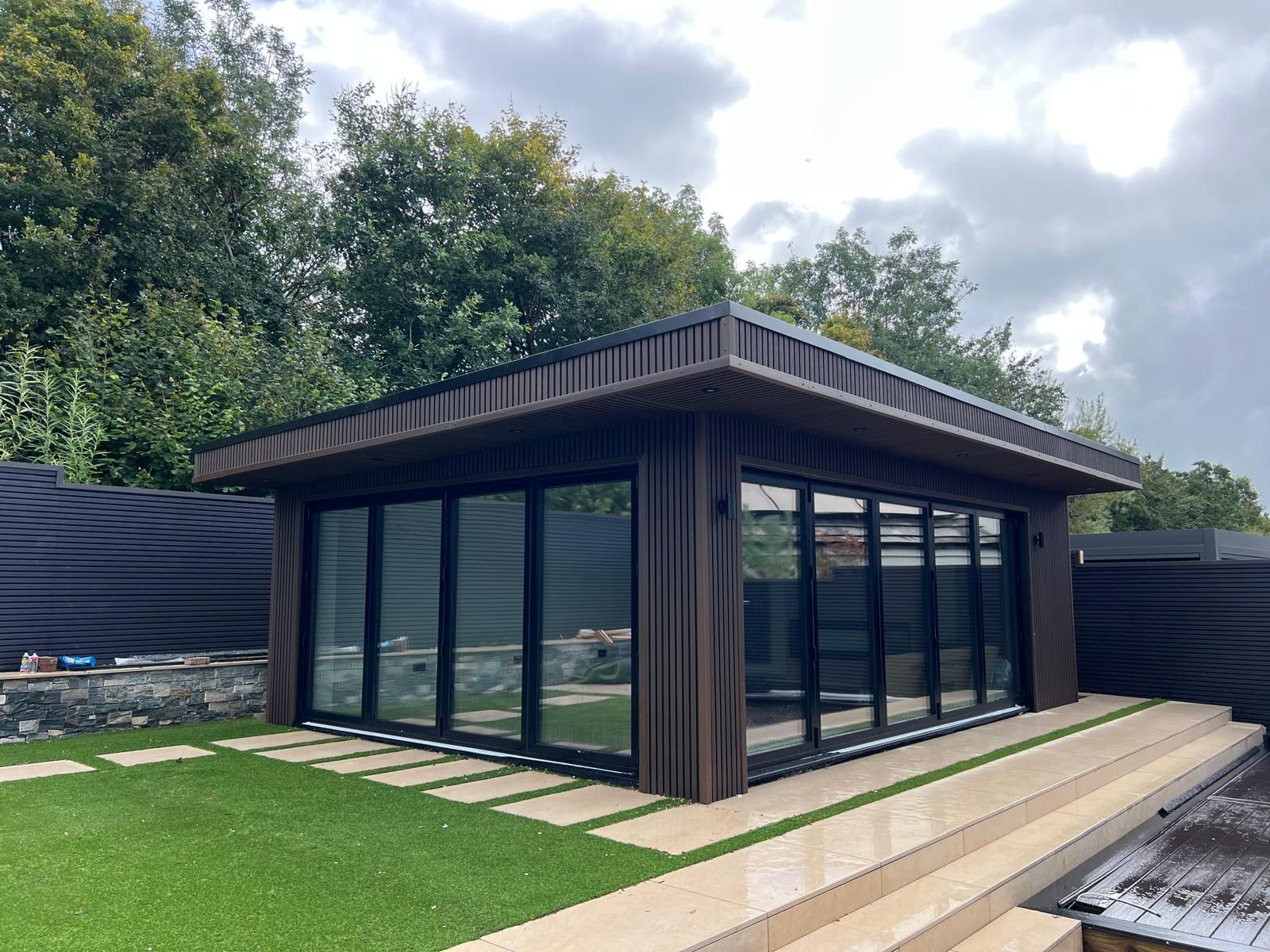 Garden Gym Room in Glasgow by Oakspan Garden gym room in Glasgow with dark timber exterior cladding, warm interior lighting, gym equipment and full-width glazing by Oakspan