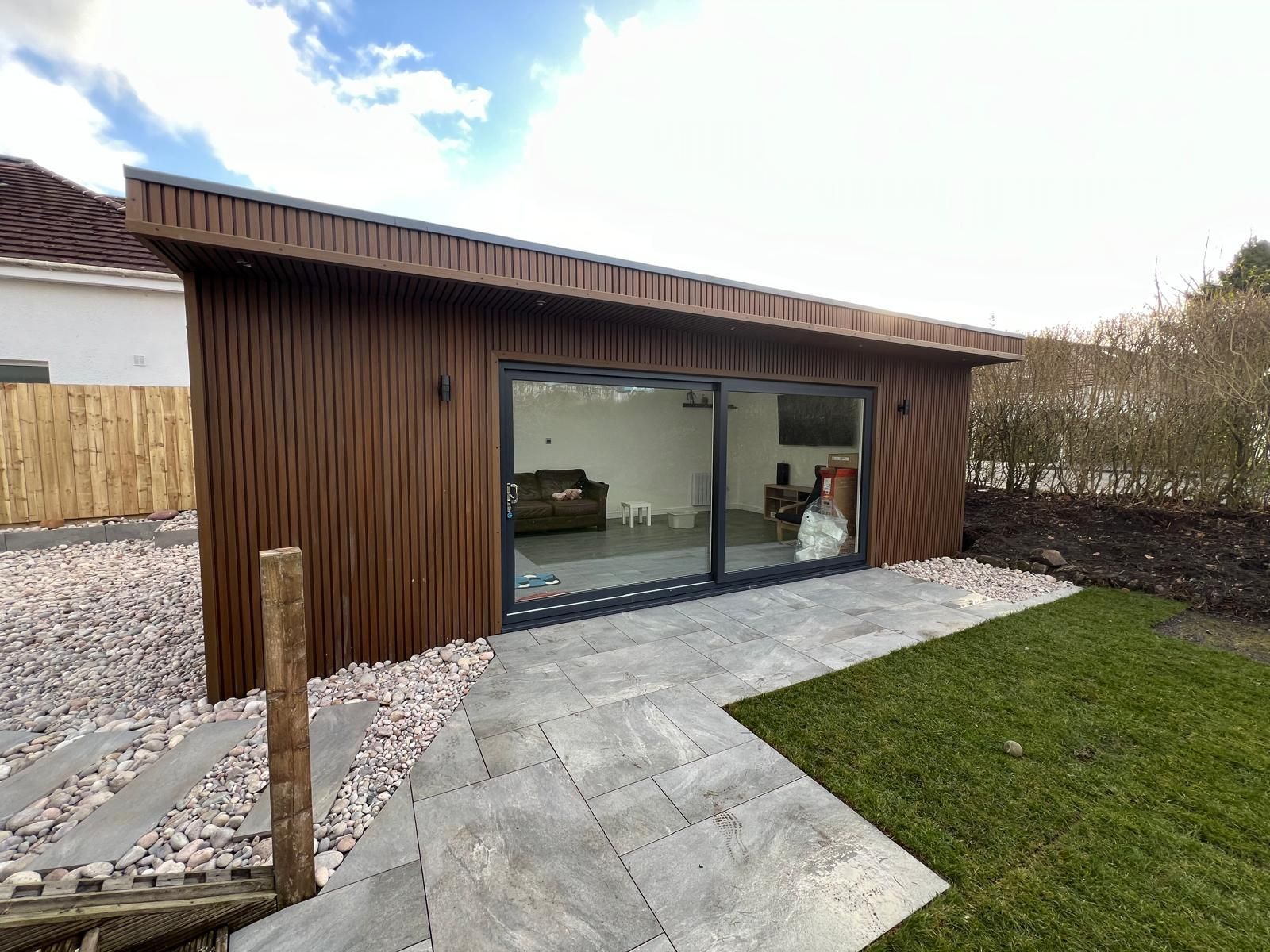 Contemporary 7x4m garden games room in Bearsden, finished with oak shadow gap composite cladding, featuring large 4m double-glazed sliding doors and surrounding landscape design by Gareth