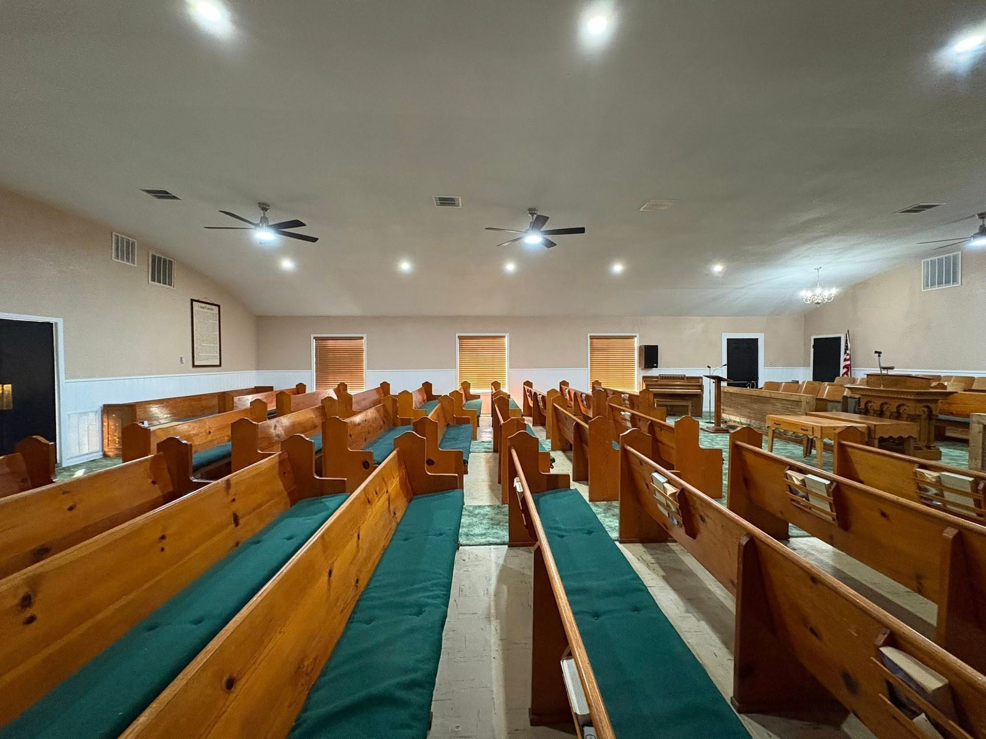 Empty church interior with wooden pews, green carpet aisle, and ceiling fans under warm lights
