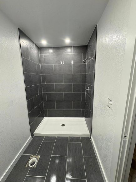 Empty tiled shower with dark gray walls, white shower pan, and recessed ceiling lights.