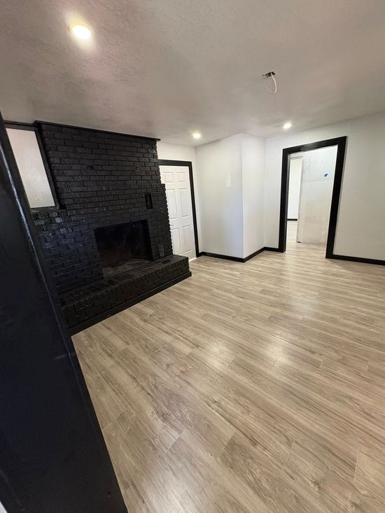 Empty room with light wood floors, white walls, black fireplace, and two doorways