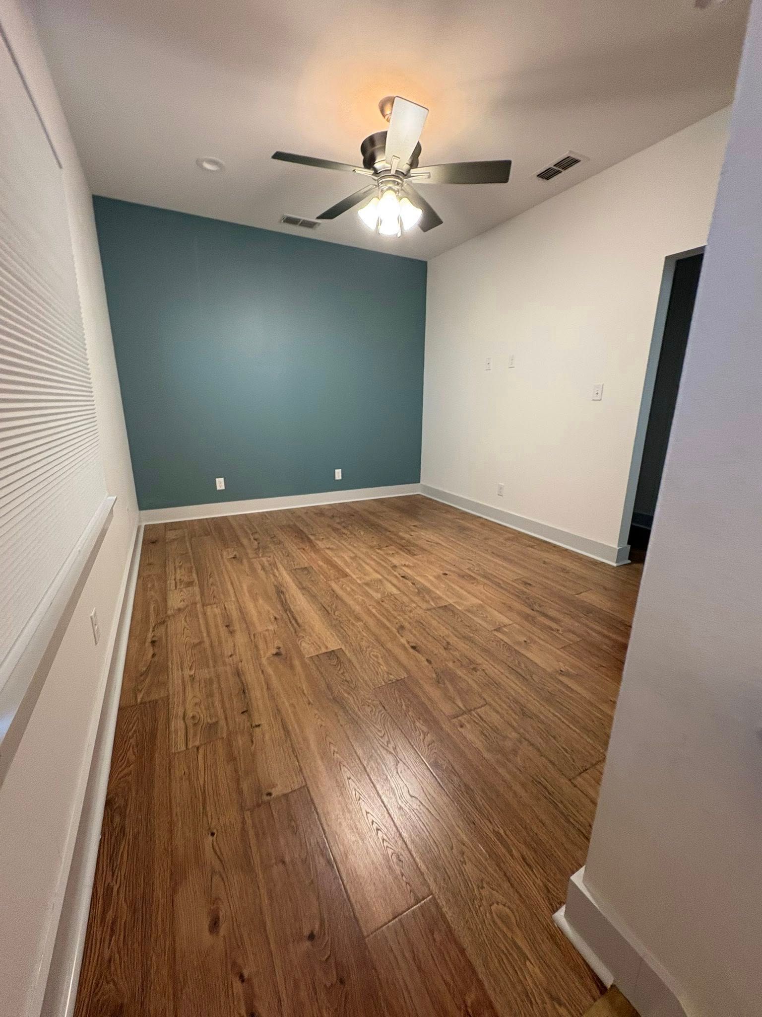 Empty room with hardwood floors, blue accent wall, white walls, and ceiling fan.