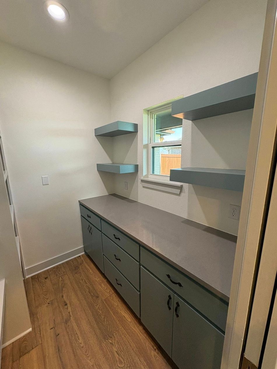 Small laundry room with teal cabinets, gray countertop, shelves, and wood-look floor.