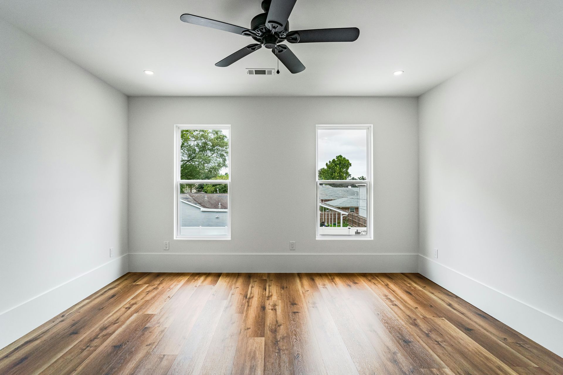 Empty modern room with white walls, wood floors, ceiling fan, and two windows