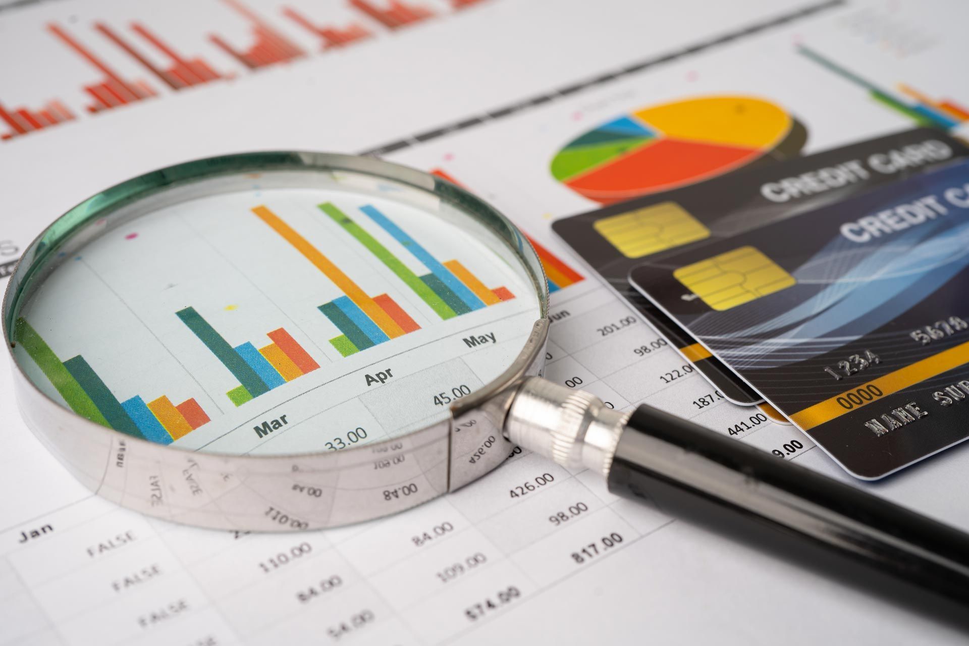 Magnifying glass over financial charts and credit cards showing data analysis.