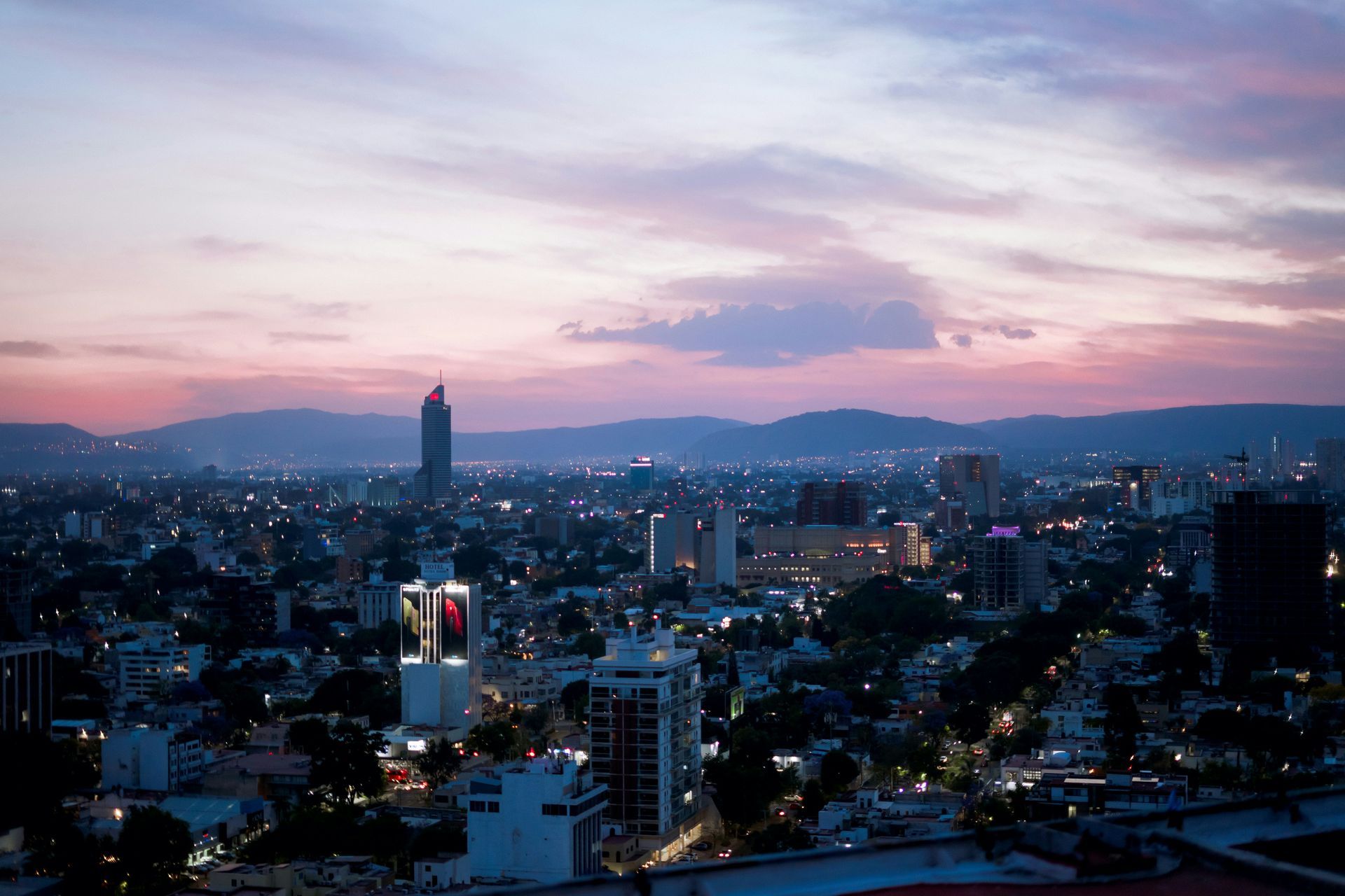 Horizonte urbano al atardecer con nubes rosadas y moradas y montañas a lo lejos.