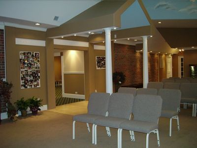Rows of grey chairs face a room with tan walls, white pillars, and a brick accent wall in a quiet, indoor space.