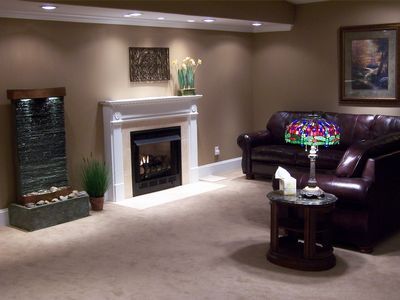 A basement living area with a fireplace, indoor fountain, brown leather sofa, and a stained-glass lamp on a side table.