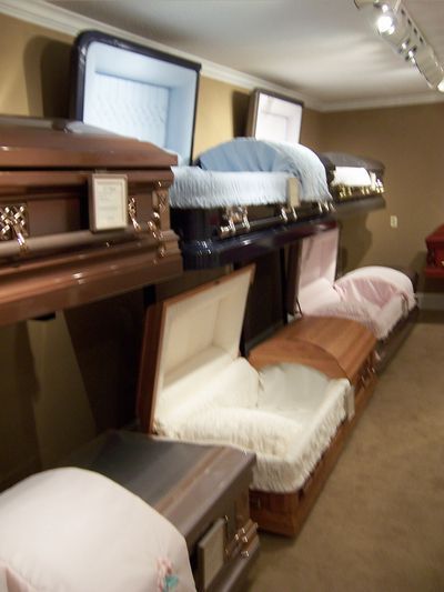 A showroom displaying a variety of open and closed caskets in different colors and materials.
