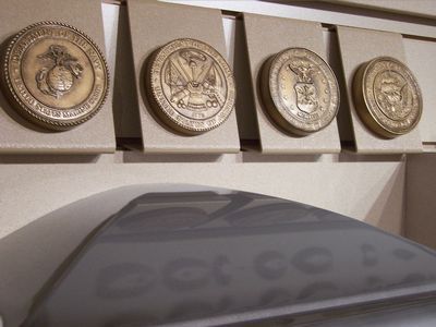 Four bronze military service branch seals displayed in a row above a dark, curved surface.