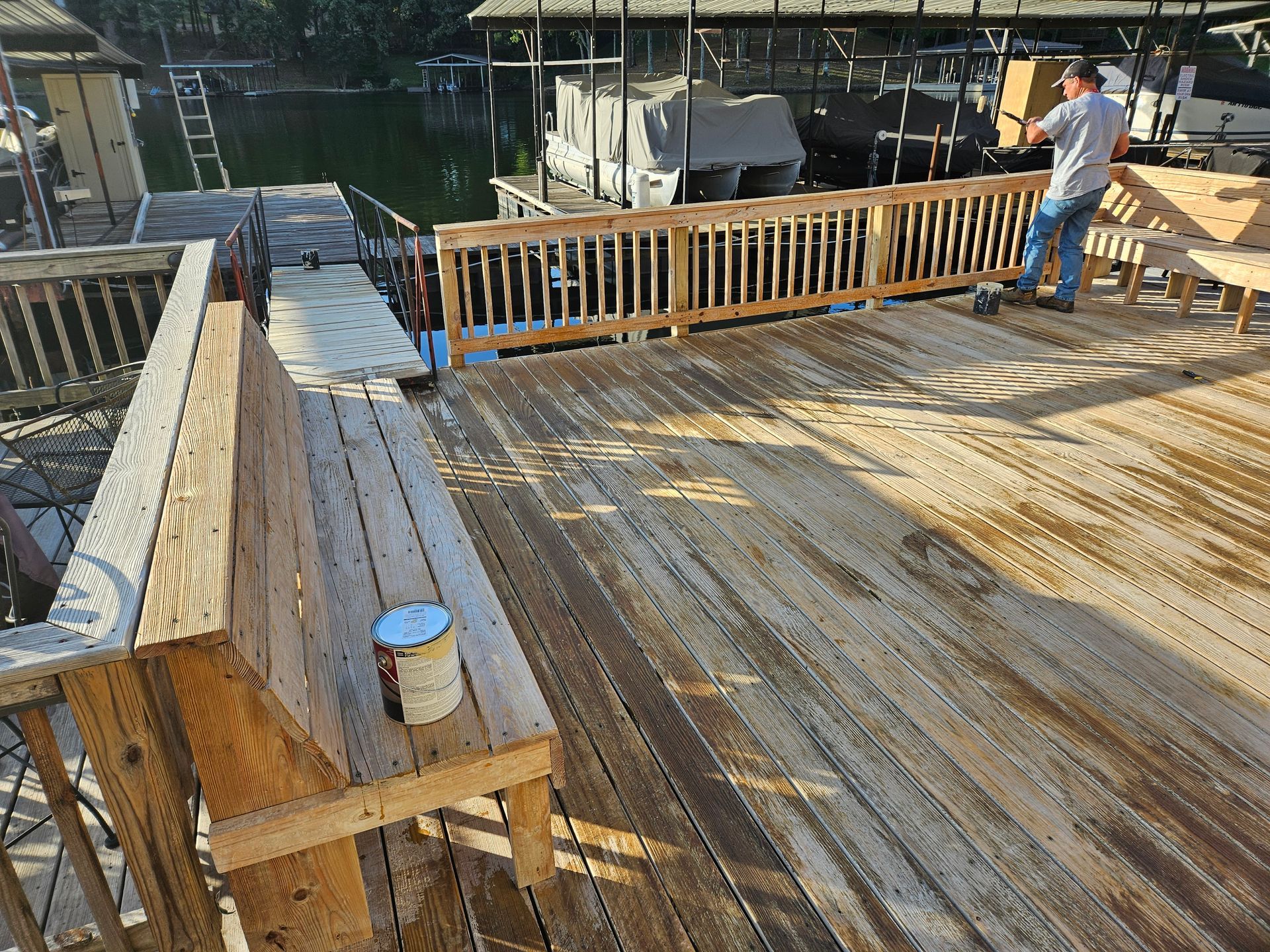 Wooden dock deck with railings by the water, with two people working near stacked materials.