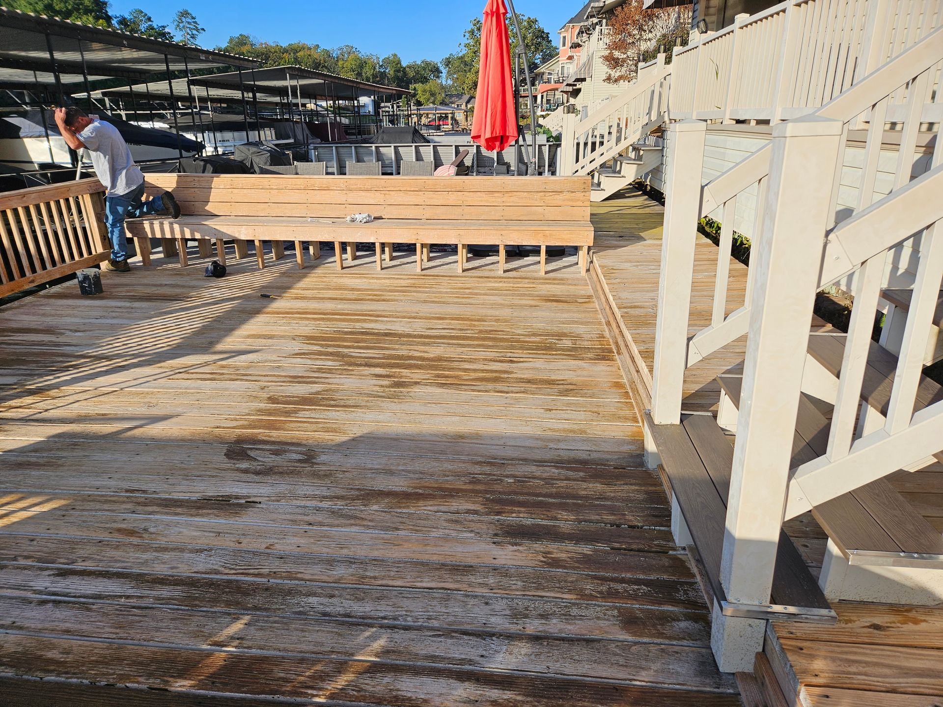Weathered wooden boardwalk with white railings and a red umbrella near a waterfront seating area