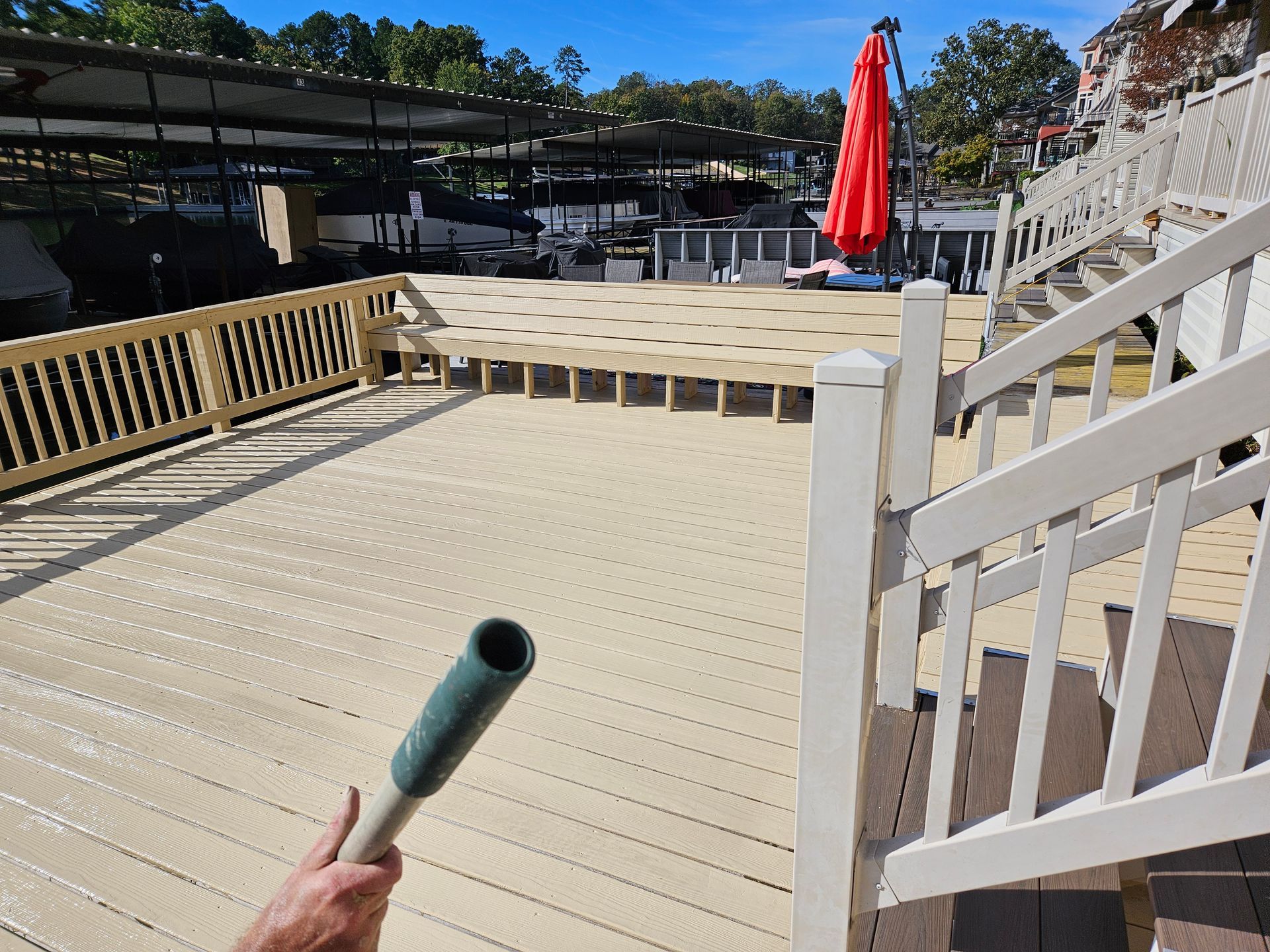 Deck with railing and stairs overlooking a courtyard, with a red umbrella and a hose in the foreground.