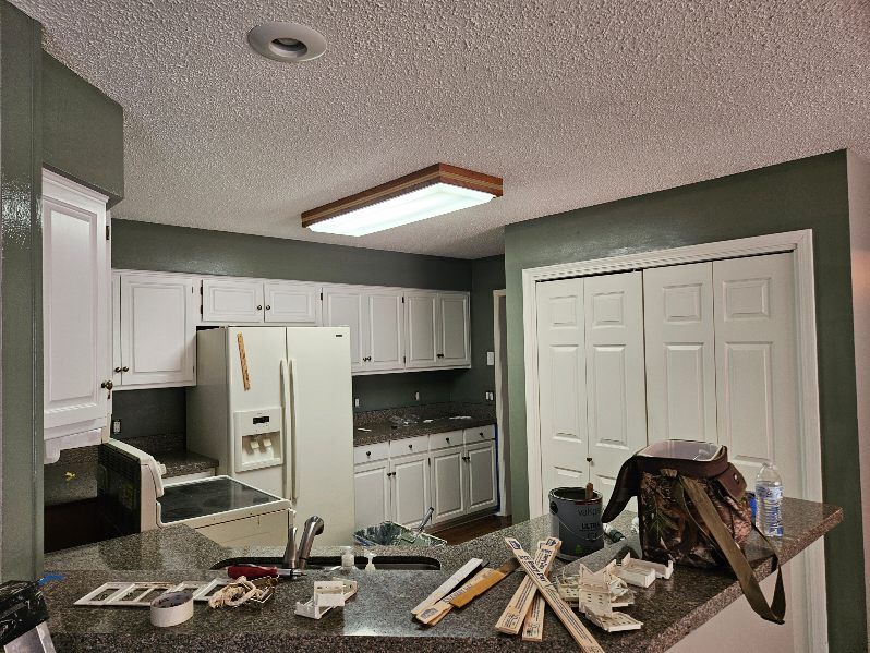 Kitchen with white cabinets, appliances, and a dark countertop with tools on it. Olive-green walls.
