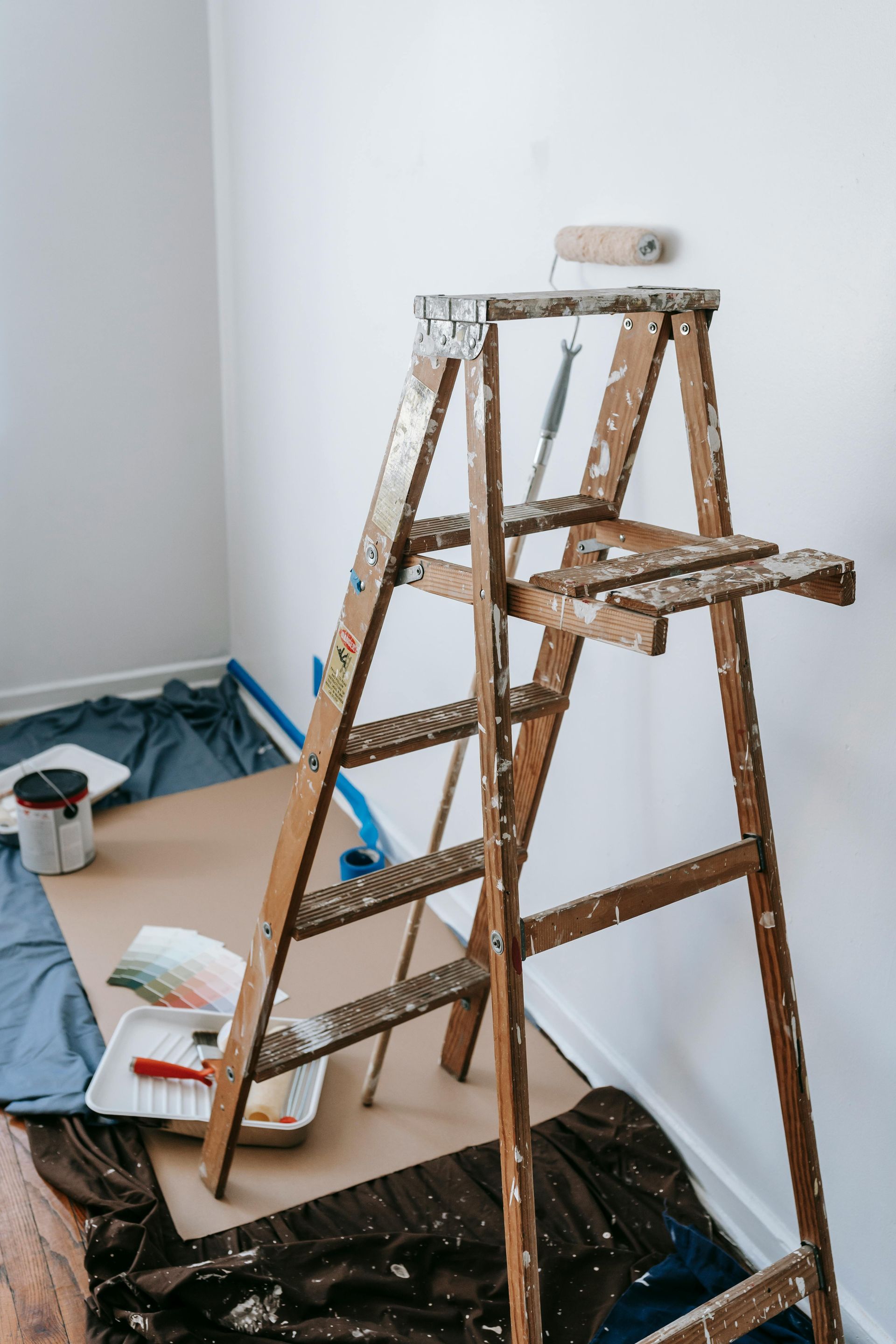 A wooden ladder in a room, paint supplies, and a partly painted wall.
