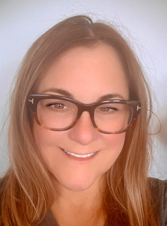 Smiling person wearing black glasses against a plain light background