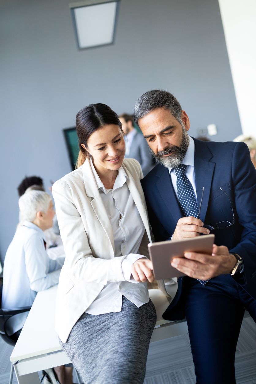 A man and a woman are looking at a tablet laying out government contract accounting details.