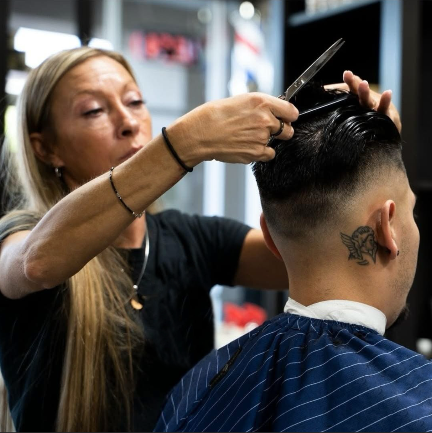 A hairstylist uses scissors to trim the top of a client's hair in a salon setting.